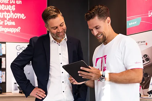 Zwei Männer im Telekom-Shop betrachten Tablet, Beratung zu Smartphones und Tarifen