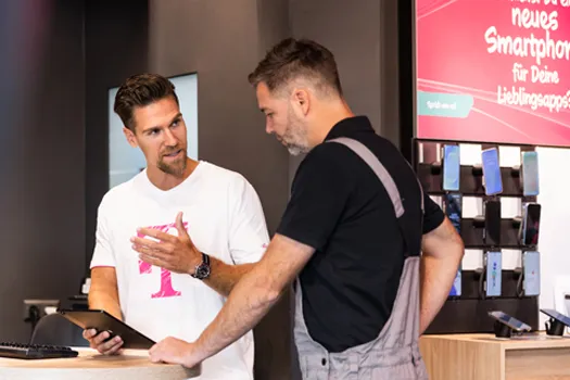 Beratung im Handyshop: Mitarbeiter zeigt Tablet, Kunde schaut auf Smartphones